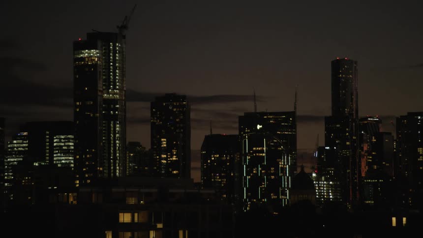 Lights glow on tall downtown buildings and towers in the darkness of night as clouds move across the sky and the sunrise brings the morning light