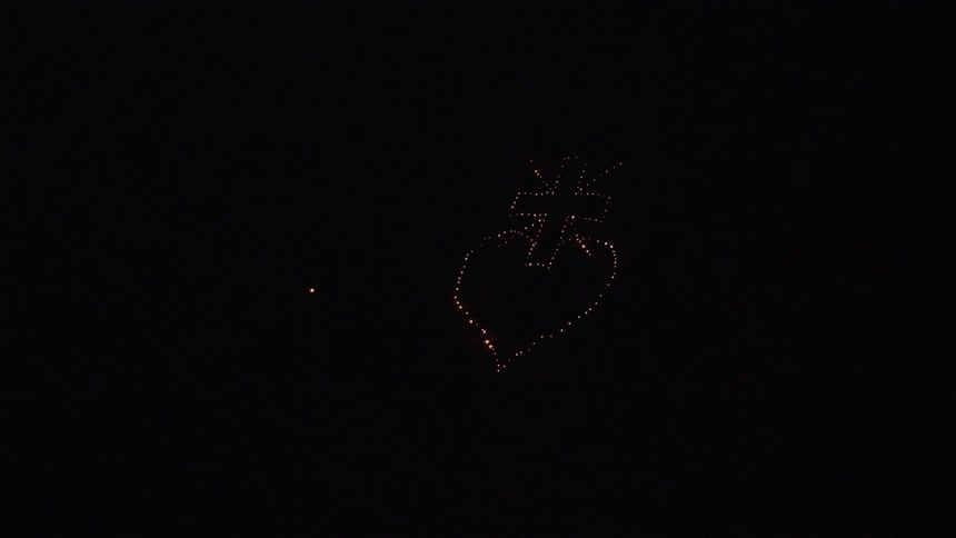 An aerial shot of a cross and heart done in lights at nighttime