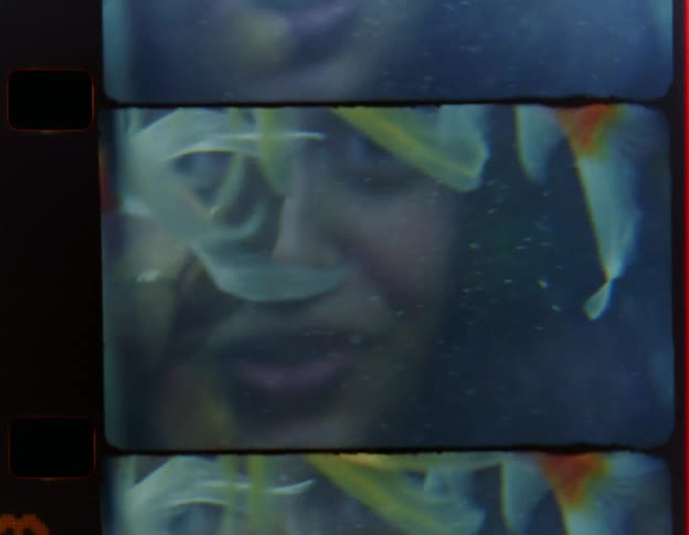 Woman smiles playfully and sticks out her tongue while looking through aquarium holding goldfish