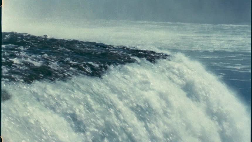 Water foams while falling down Niagara Falls waterfall towering over misty surroundings