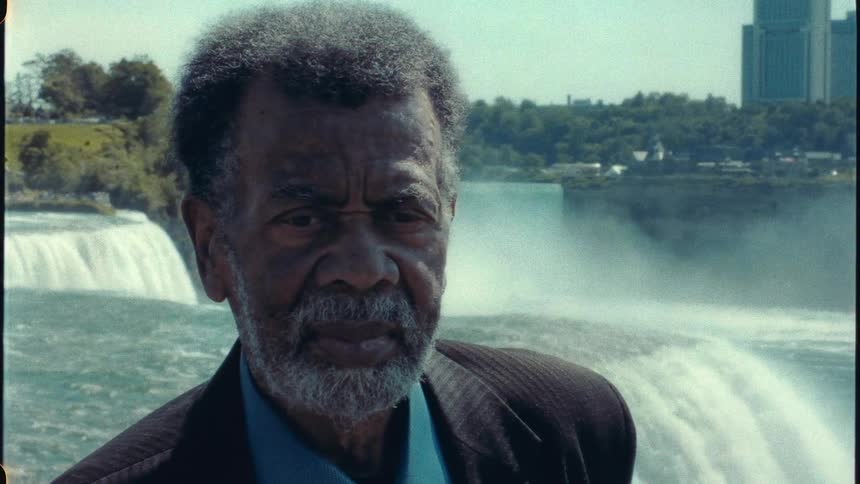 Close up of the face of a man standing in front of Niagara Falls waterfall next to the city looking at the camera