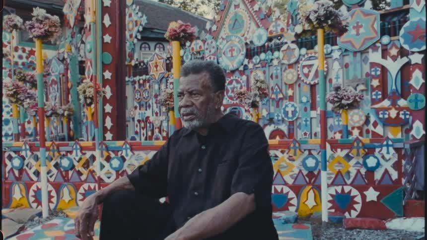 A man sitting outdoors in a colorfully painted area while he sits staring ahead