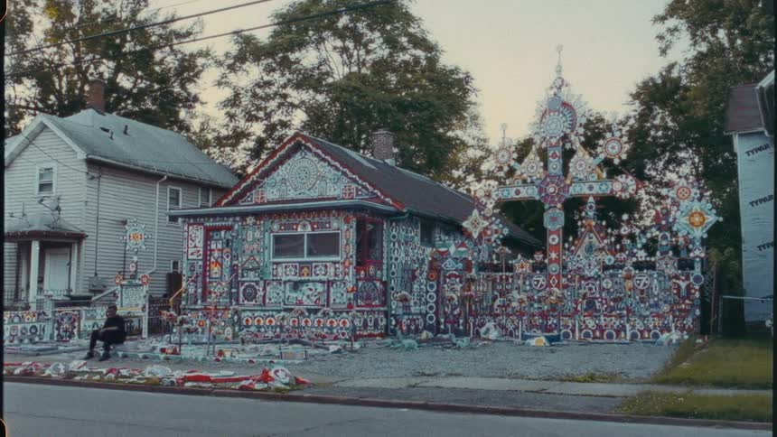 A man sits on the stoop in front of an artistically designed house on a suburban street