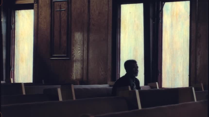An older man sitting in a church pew alone looking forward and thinking