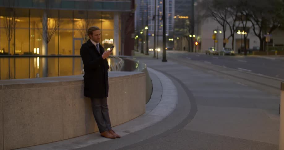 Man stands in city at dusk checks his phone