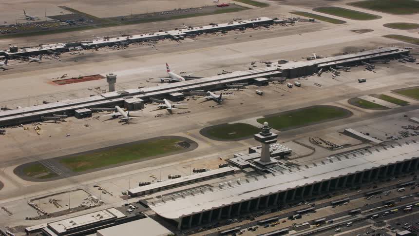 Airplanes are parked at an airport as traffic moves on the road and around the airport