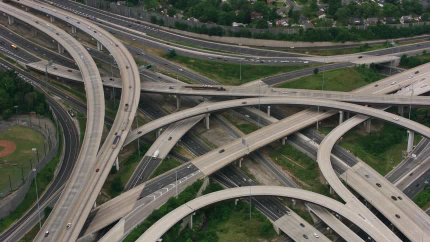 Traffic flows along overlapping overpasses and highways near baseball fields and houses