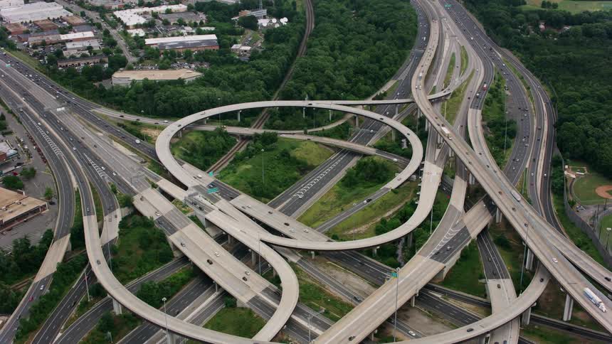 An aerial of a highway junction with on and off ramps with traffic traveling the roads near a suburban neighborhood