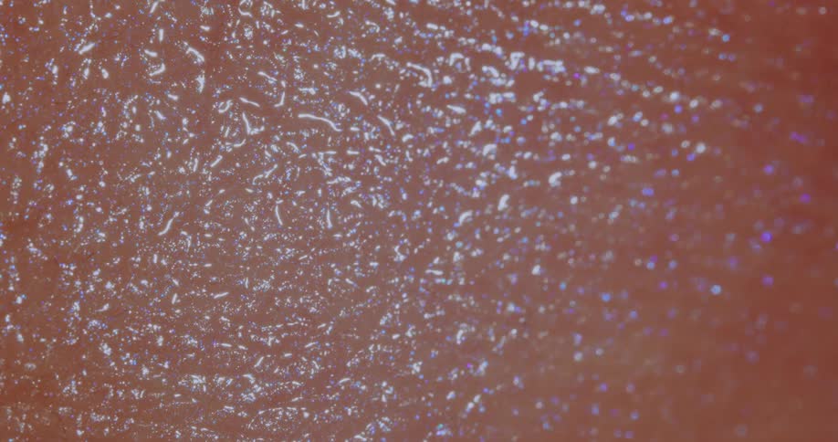 Light shines on a wet glittering substance as it sparkles on a pink surface