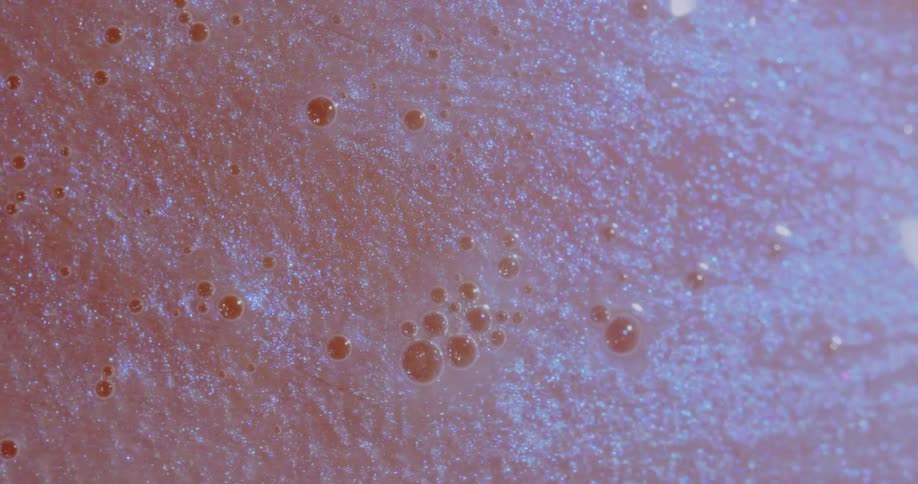 Light shines on a sparkling liquid as it moves over a pink surface around small dark orbs