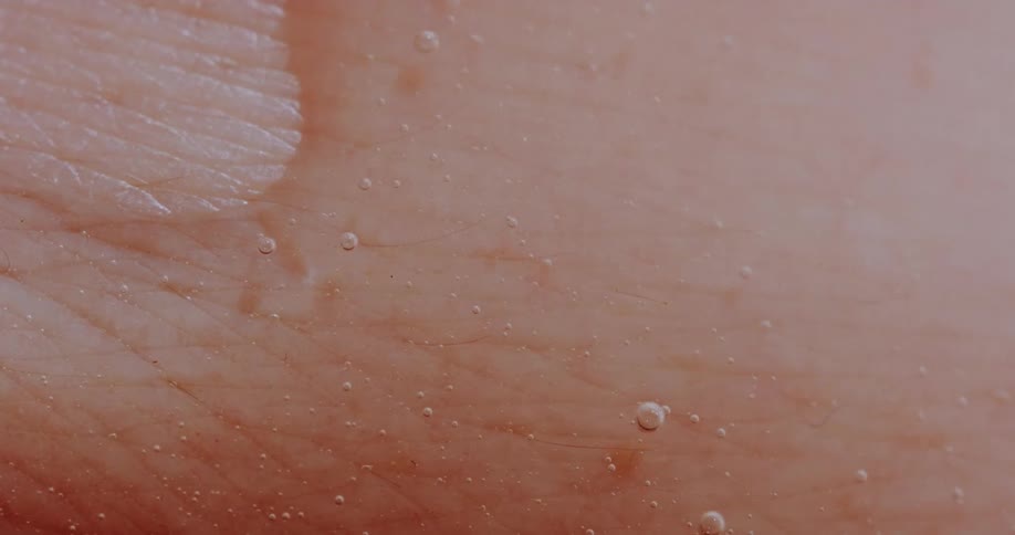 Liquid soap going over human skin with tiny soap bubbles popping in it