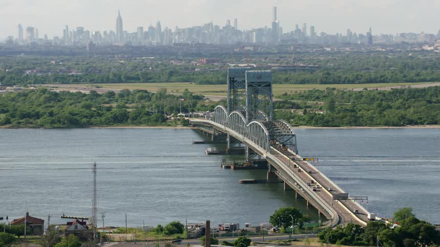 Vehicles drive down a bridge over a river near downtown