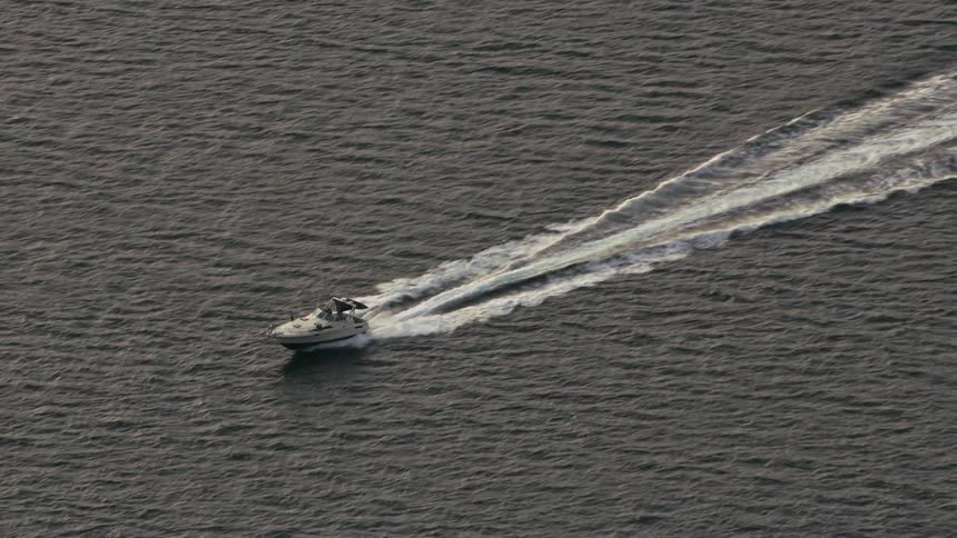 An aerial of a boat driving on the ocean creating waves behind it on the rough waters