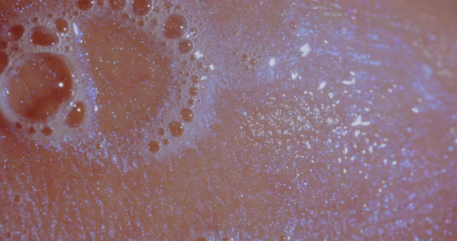 Larger soap bubble pops on surface of peach gleaming mixture