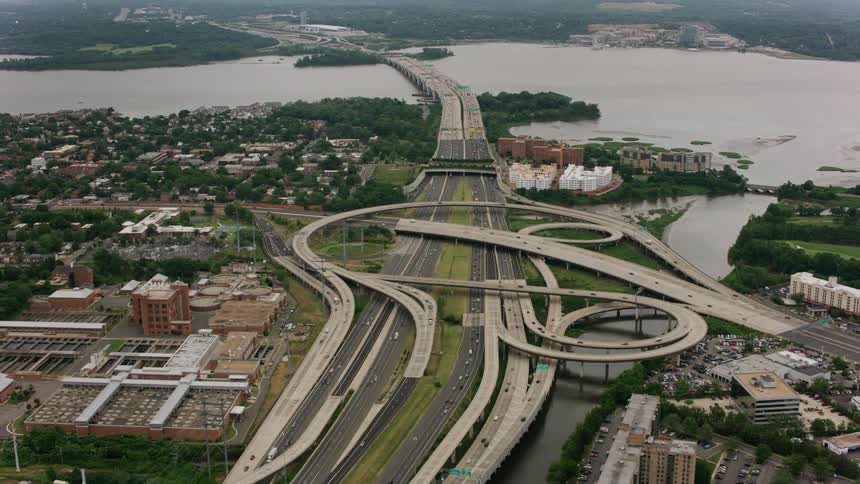 Traffic moves on a super highway junction around curves and bridges along the coast near buildings in a town