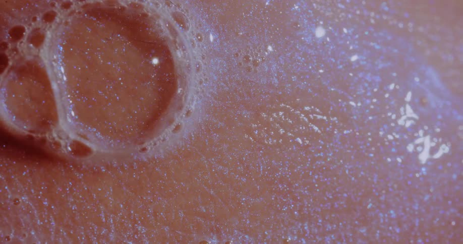 Soap bubbles foam among slowly flowing reflective liquid on peach surface