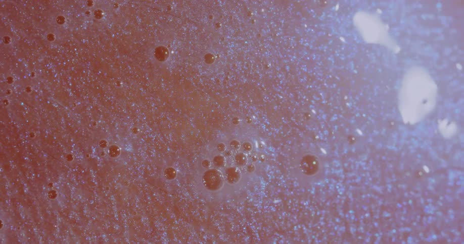 Light shines on a sparkling liquid as it moves over a pink surface around small dark orbs