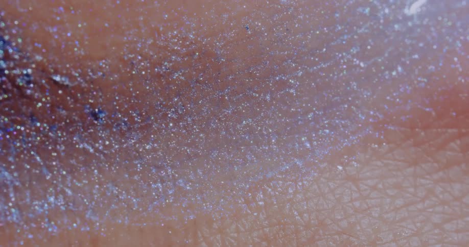 A sparkling glittering liquid substance moves over a pink textured surface as it twinkles in the light