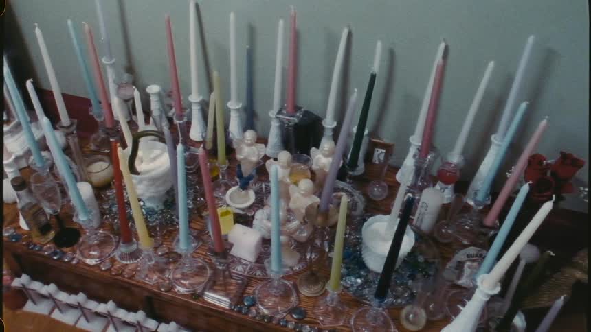 Multiple candles some in religious themed shapes over surface of altar decorated with polished stones