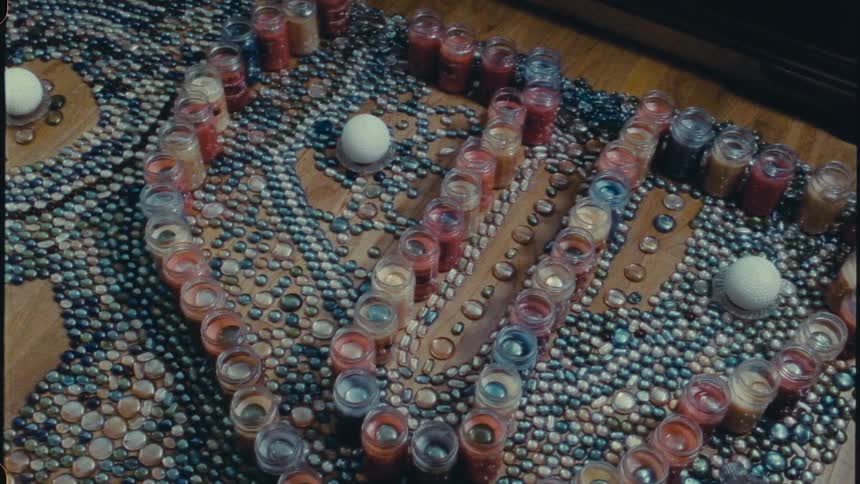 Jars filled by various colors form pattern around candles with polished stones on a wooden surface