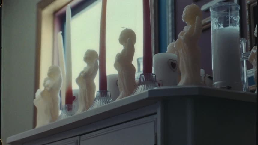 A dresser under a window with many candles on it some of which are shaped like angels