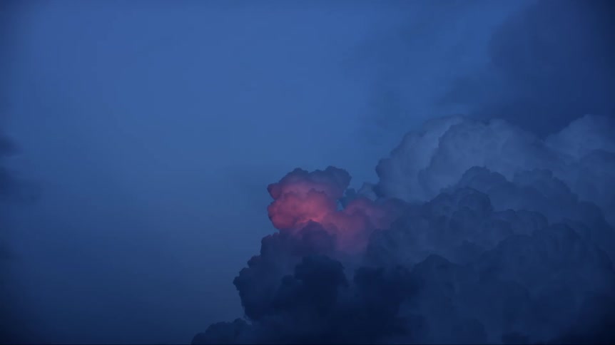 Pink light reflects on cumulus clouds in a darkening blue sky