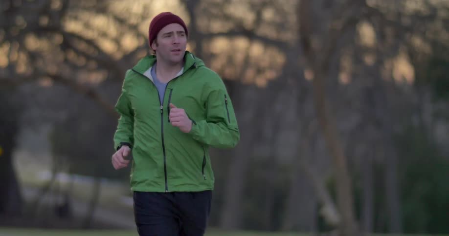 A man jogging down a tree lined street in the winter at sunset