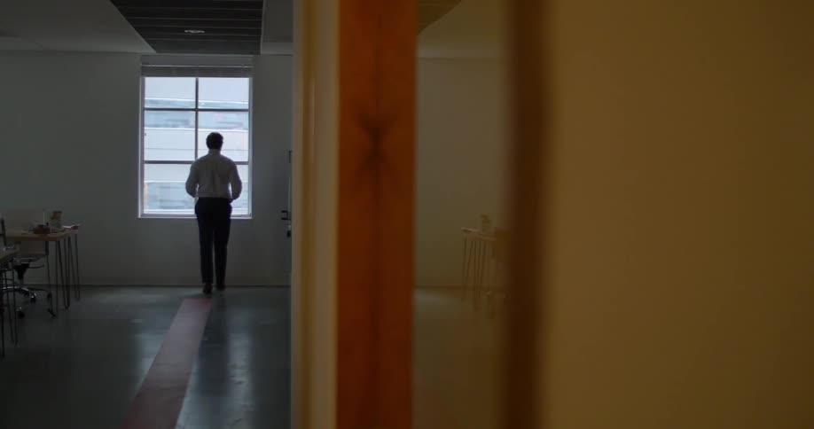 A man walking through a house and stopping to look out a window