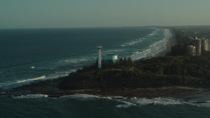 Waves crash onto the shore below a lighthouse near downtown