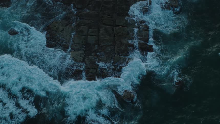 Drone view looking straight down at waves crashing against and over rocks along the coast