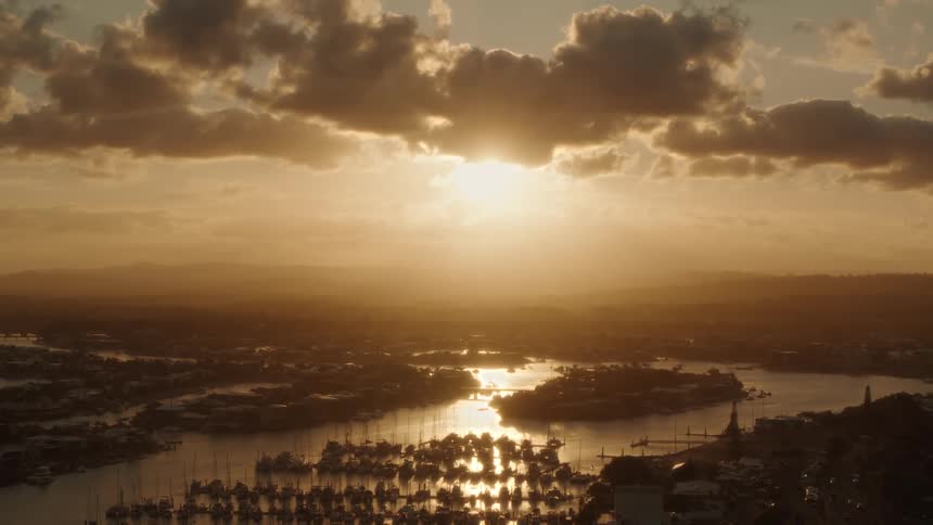 Drone view of the sun setting in the evening over a boat marina as light reflects off the water