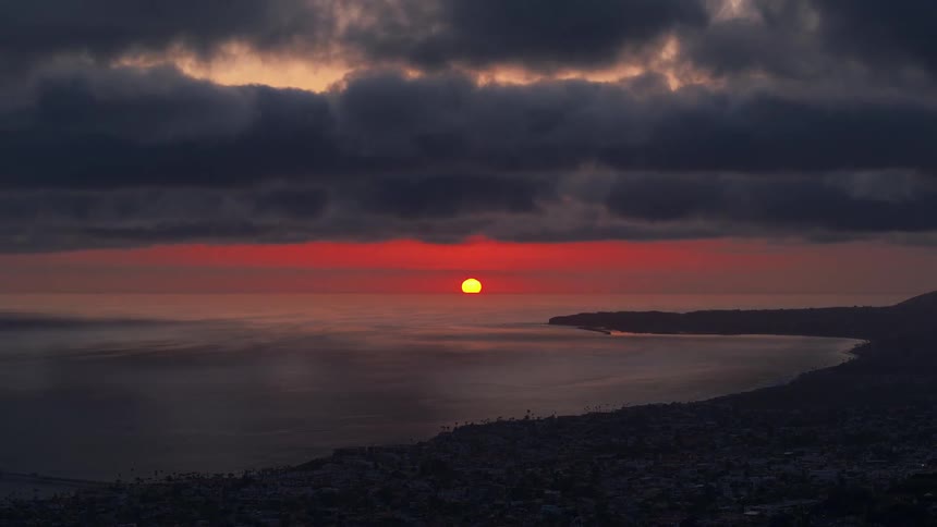 A time lapse of the sun setting on the pink horizon and waves roll onto the beach and clouds roll across the sky