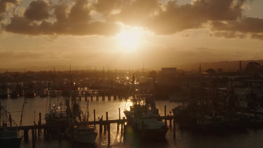 Boats are docked in a marina as the sun shines brightly in a cloudy sky and sunlight reflects on the water