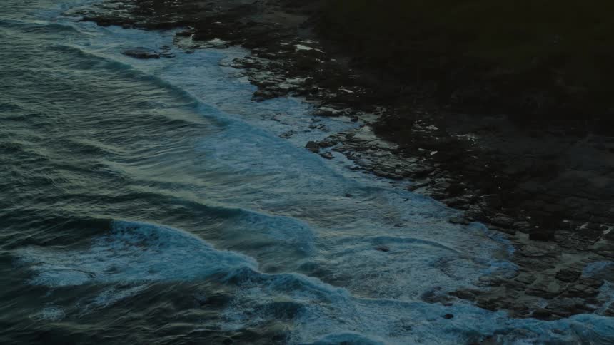 Waves roll into shore and splash against the rocks along the coast