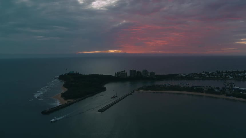 The sun sets as a boat sails from a canal in to the ocean