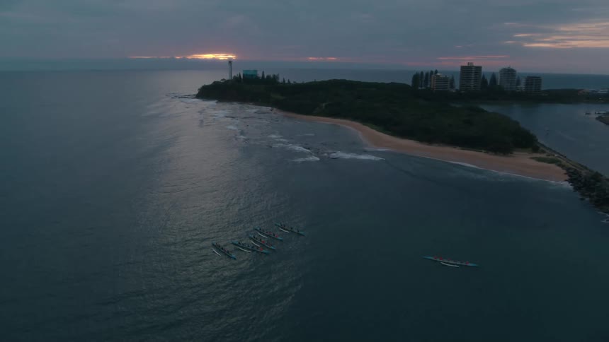 Outrigger canoes float a short distance from forested coast near high rises