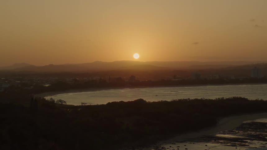 The sun beginning to set behind mountains over a lake