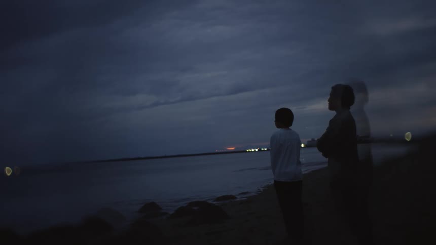 A man and child are standing on the beach at sunset