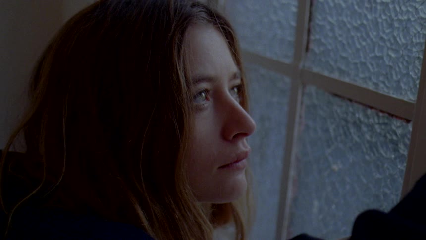 An up close of a womans face with hardly an expression on it next to framed windows