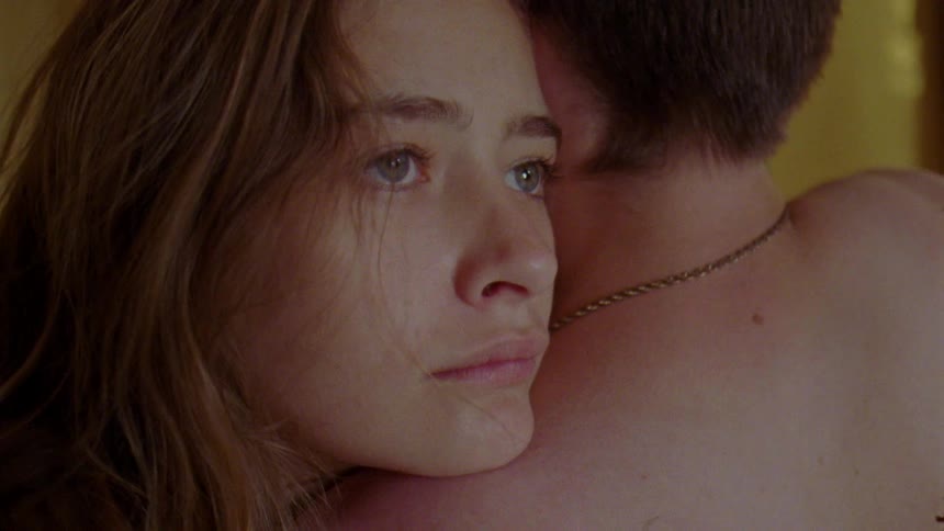 A close up of a womans face with a sad expression resting on a mans bare shoulder