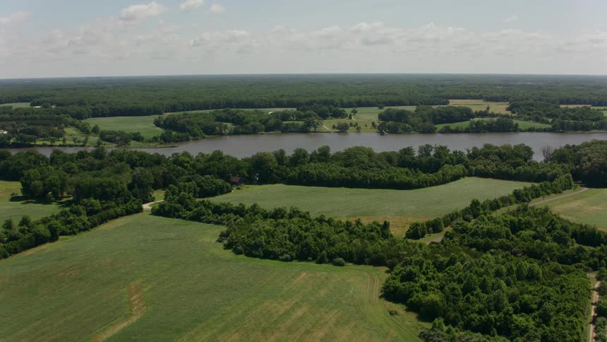 A travelling shot of farmland from a field to grass to a lake and a forest beyond