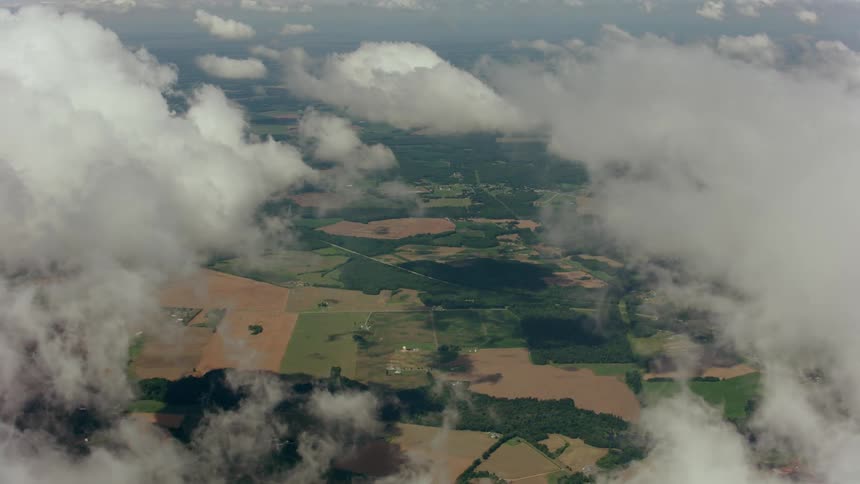 An aerial view of a large plain of fields and crops as seen between dense clouds