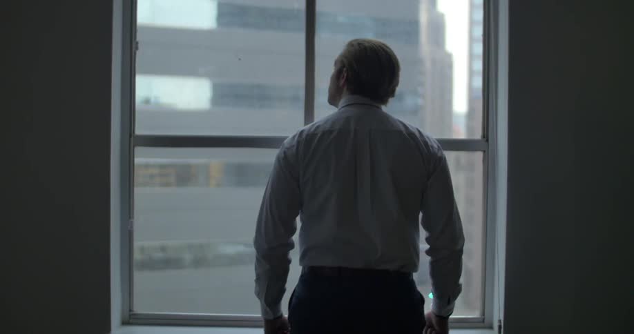 A man stands at a window looking around at the city beyond the glass