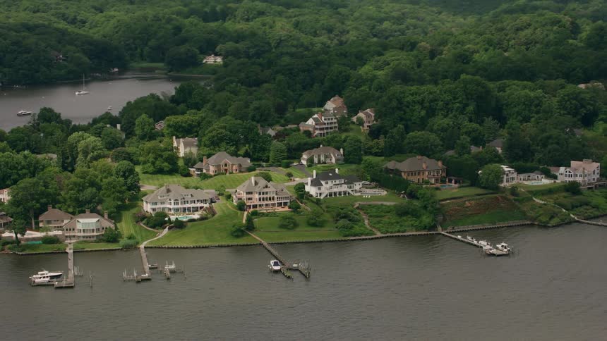 A small neighborhood of mansions outside of woods along the coast with boats docked in the water under a hazy sky