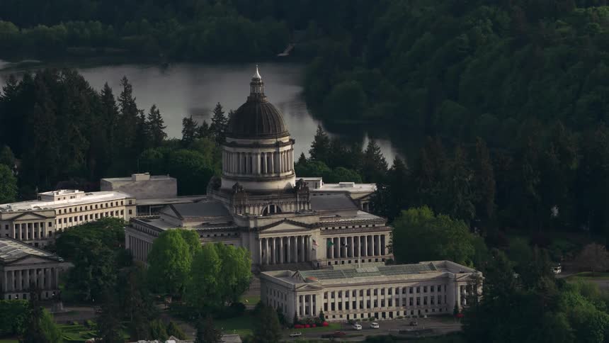 A large building with a domed tower at the edge of a city separated from a forest by a river