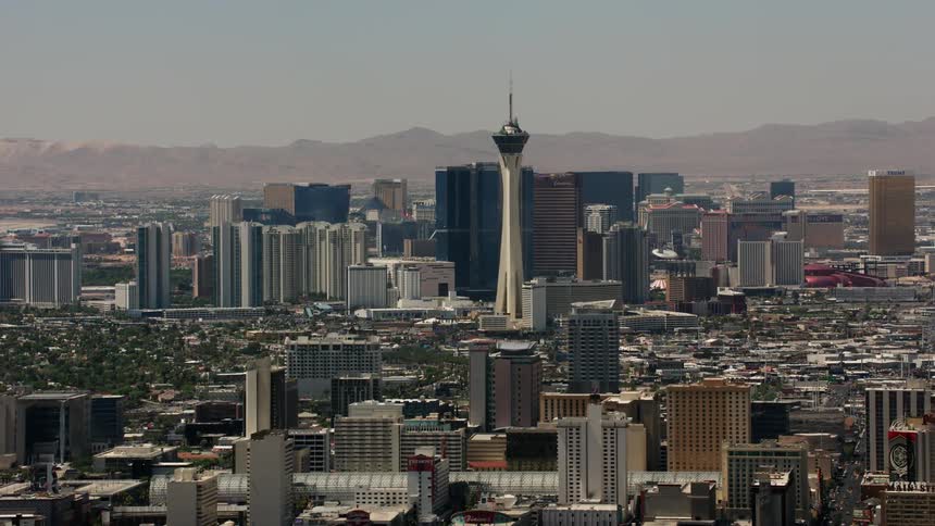 A unique tower stands tall on the skyline with buildings and skyscrapers and mountains in the distance