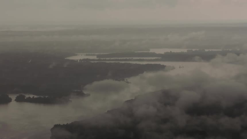 View through clouds and fog of a swampy lake with trees and woods on the surrounding land