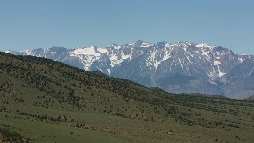 Snow capped mountains sit behind shrub covered hills