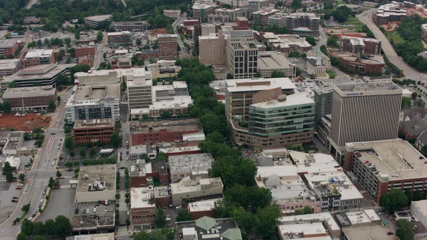 Traffic moves through a city streets with many buildings and cars in parking lots