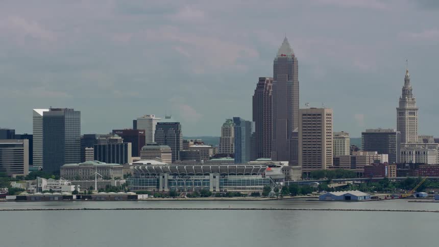 Boats sail in the lake as traffic moves on the highway outside a city along the coast with tall buildings and skyscrapers on the skyline